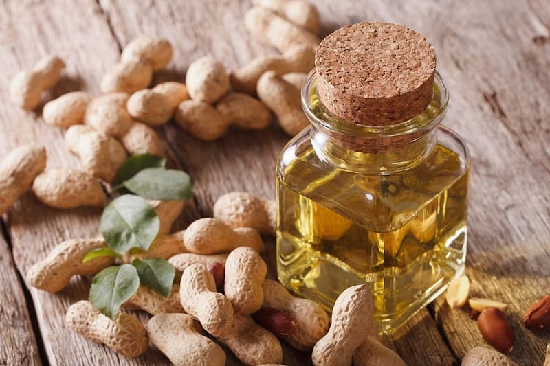 تعدادی بادام زمینی و روغن گرفته شده آن در ظرف شیشه ای